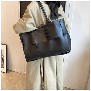 Detail of black woven leather tote bag with large square pattern on model's shoulder