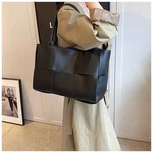 Detail of black woven leather tote bag with thick strap on khaki trench coat shoulder