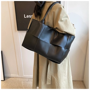 Side view of large black woven leather tote bag with wide straps on a trench coat