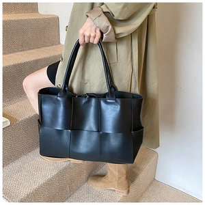 Close-up of black wide woven faux leather tote bag showing detailed texture and strap