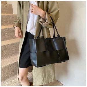 Detailed view of large black woven leather tote bag shown on a model for city commute