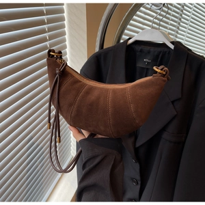Detailed close-up of brown suede croissant bag with stitching and drawstring shoulder strap