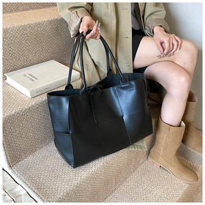 Close-up of black woven tote bag with large square pattern on a stylish city model