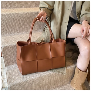 Detail of a large brown woven leather tote bag with thick weave texture and long straps