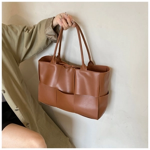 Detail of a brown woven tote bag featuring wide-strip weaving and a bow tie closure