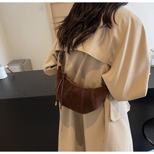 Detail of a dark brown suede croissant bag with decorative stitching on a trench coat