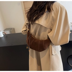 Detail view of a brown suede croissant bag on a model wearing a beige trench coat