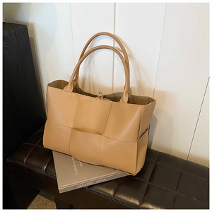 Detail of camel woven leather tote bag texture on a luxury bench with soft lighting