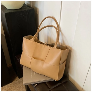 Detail of a large woven tote bag in khaki leather placed on an elegant indoor bench