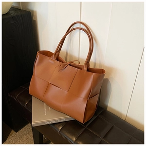 Detail of dark brown woven tote bag featuring wide leather weave on a minimalist bench