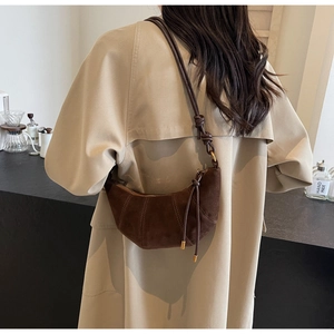 Detail shot of a dark brown suede crescent bag worn by a model in a khaki coat