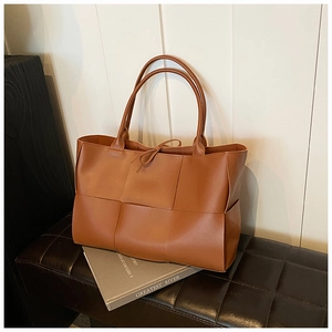 Close-up of caramel brown woven tote bag featuring wide leather weave on quilted bench