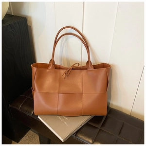 Detail of a brown woven leather tote bag featuring large plaid texture and tie closure