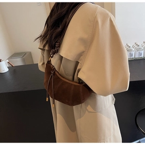 Close-up of a dark brown suede crescent bag with knot detail worn by a model in a trench coat