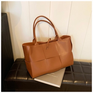 Detail of a brown woven leather tote bag with large square patterns on a black bench