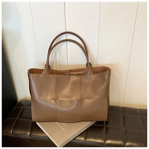 Detail of dark brown woven tote bag with wide leather straps on a vintage leather bench
