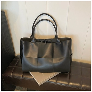 Detail of black woven tote bag with large square weave pattern and minimalist top handles