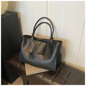 Detailed close-up of large black woven leather tote bag with stylish square weave pattern