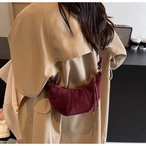 Close-up of burgundy suede croissant bag with vertical stitching and knot shoulder strap