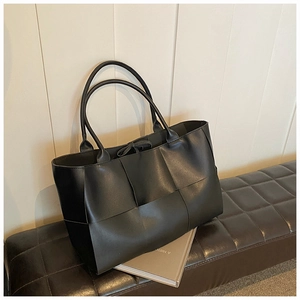 Detail of a large black woven tote bag made of high-quality faux leather on a bench