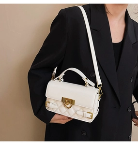 Detail of white quilted leather handbag with gold twist lock and chain on black blazer