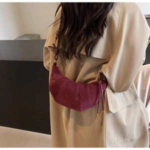 Detail of burgundy suede croissant bag with knotted strap and gold metal hardware
