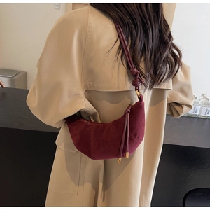 Detail of burgundy suede croissant bag with unique knot shoulder strap on trench coat