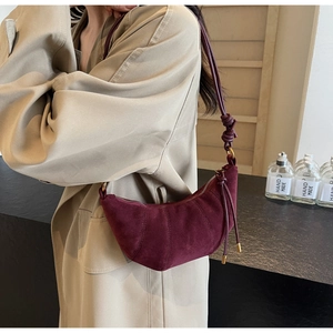 Detail of burgundy suede croissant bag with pleats and slim strap on shoulder