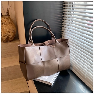 Detailed view of dark brown wide-woven leather tote bag on wooden steps