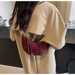 Detailed view of burgundy suede crescent bag on a model wearing a beige trench coat