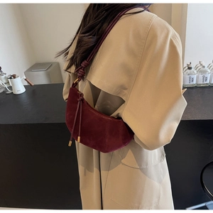 Detail of burgundy suede croissant bag showing knot shoulder strap and vertical stitching