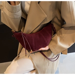 Close-up of burgundy frosted suede crescent bag with segmented stitching and metallic tips
