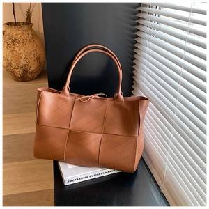 Macro detail of brown woven leather tote bag featuring large grid texture and slim handles