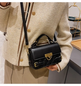 Detail view of black quilted leather handbag with gold hardware and chain on a model