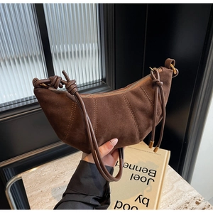 Detail of dark brown suede crescent bag featuring vertical stitching and knotted strap