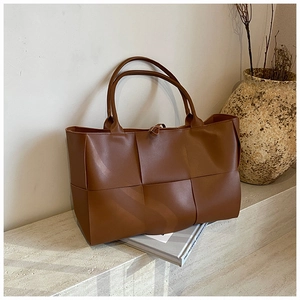 Detail of premium brown woven leather tote bag placed on a textured stone surface
