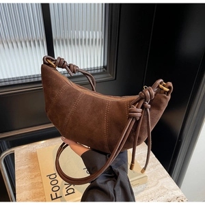 Close-up of dark brown suede crescent bag featuring vertical stitching and knotted strap