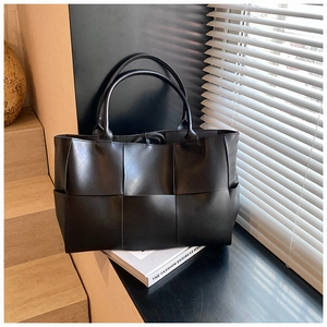 Detailed close-up of a black woven leather tote bag on decorative books with shadows
