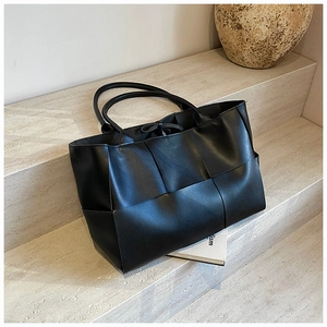 Detail of black woven leather tote bag with thick strap weave on stone steps background