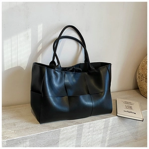 Close-up of black woven large tote bag with wide leather straps on stone steps