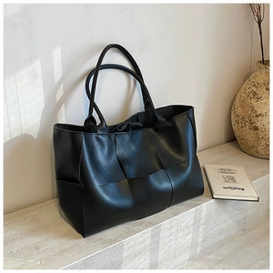 Detail shot of large black woven leather tote bag with thick crisscross texture on stone