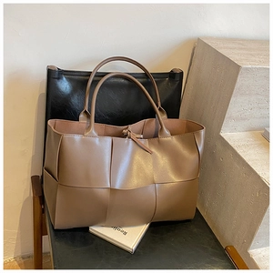 Detail of a large woven tote bag in clay brown faux leather on a black chair