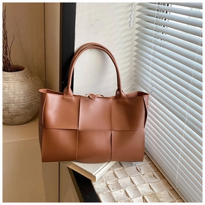Close-up of large woven caramel tote bag showing the wide leather weaving craftsmanship