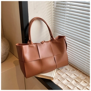 Detail of brown woven leather tote bag showing large plaid texture in natural window light