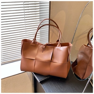 Detail of caramel brown woven tote bag featuring decorative bow and long top handles
