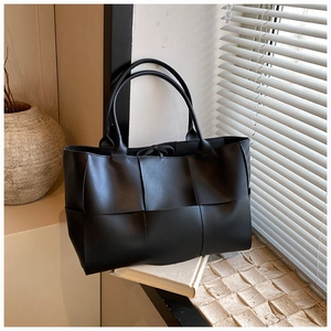 Macro view of black leather woven tote bag featuring thick interlaced strips and round handles