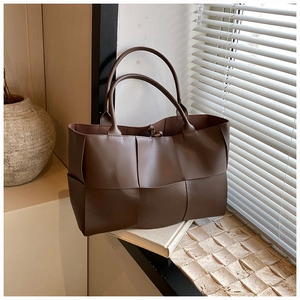 Detail view of dark brown woven tote bag with wide leather straps in a minimalist setting