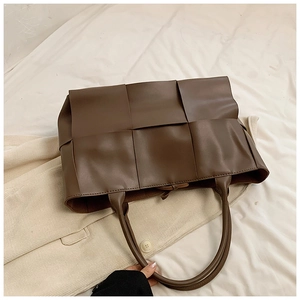 Top-down view of a dark brown large woven tote bag with wide straps on white fabric