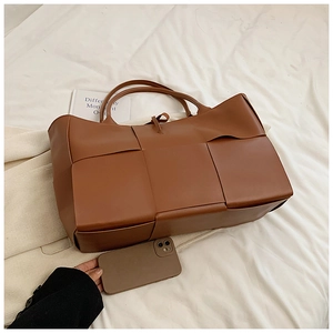 Detail of large brown woven tote bag showing the wide leather strips and spacious design
