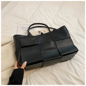 Detail of black woven large tote bag with wide strips and interior lining on white fabric